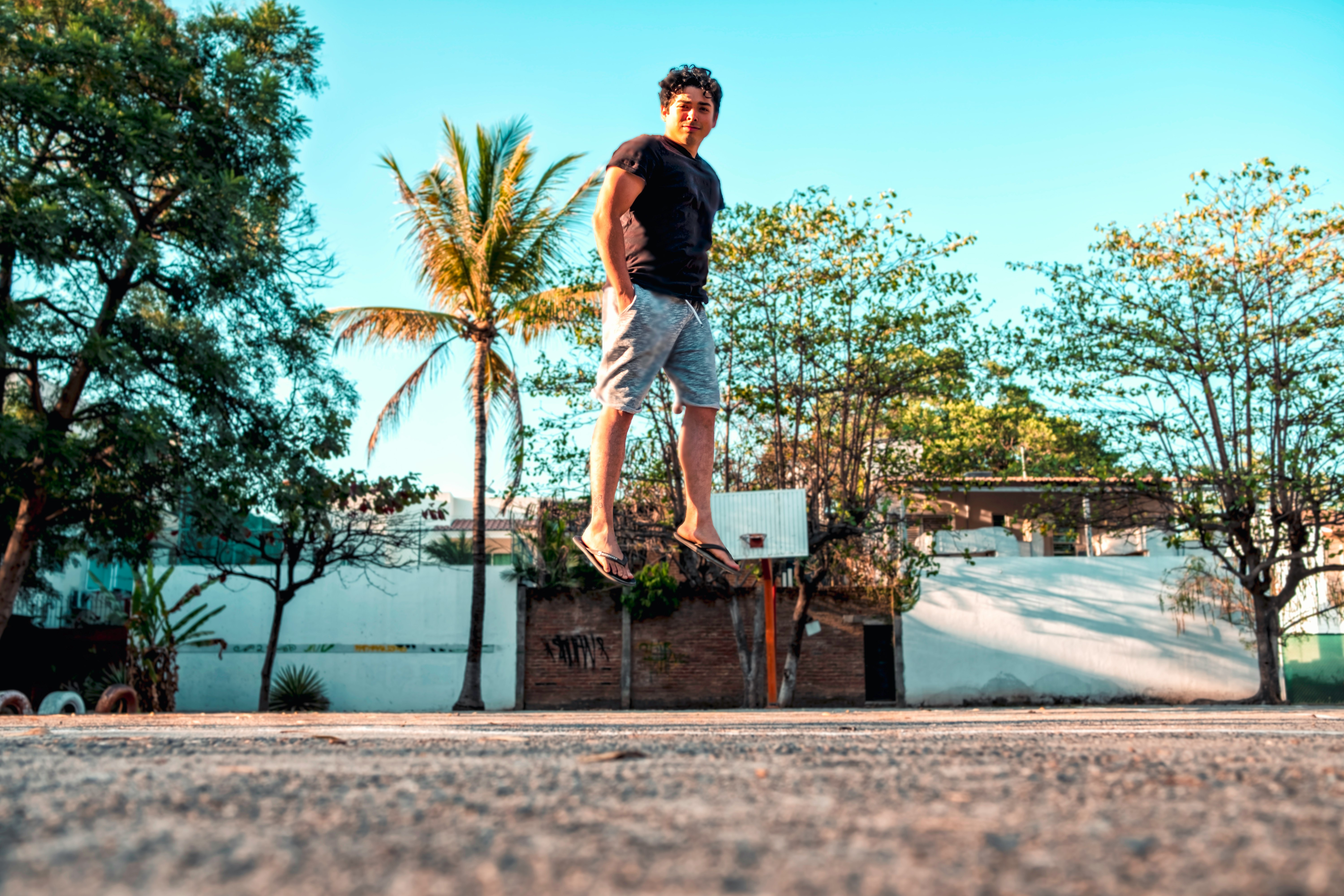 low angle photo of man standing on concrete ground beside trees